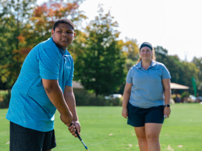 Young man holding club with coach watching.